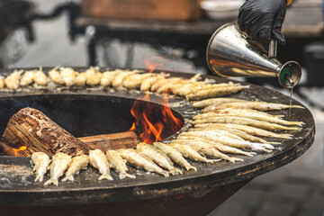 Preparing traditional tasty fried fish being cooked on an open fire in a street food market, ready...
