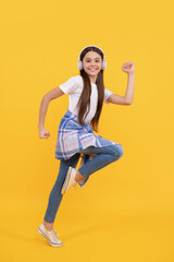 Fototapeta na wymiar Energetic teenage girl running while listening to music in headphones yellow background, fun