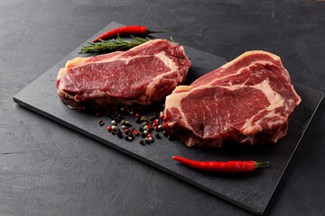 Two classic raw beef steaks with red hot peppers on a cutting board