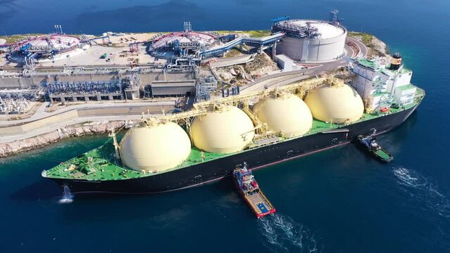 Aerial drone rotational video of LNG (Liquified Natural Gas) tanker anchored in small gas terminal island with tanks for storage