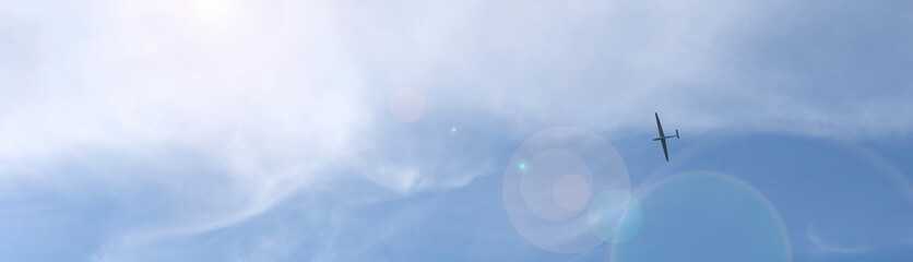 A glider plane in blue cloudy sky low angle photography.As banner with lens flare.