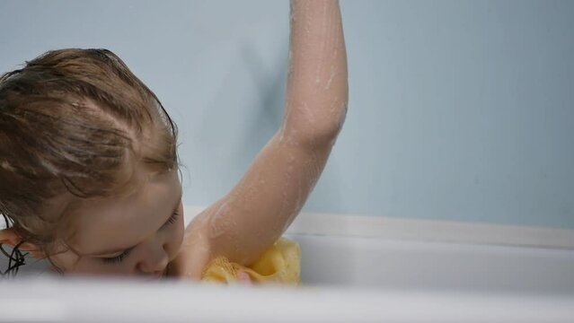 Portrait. a little preschooler takes a bath on her own, soaps herself with a washcloth while sitting in the bath. Slow motion, close up