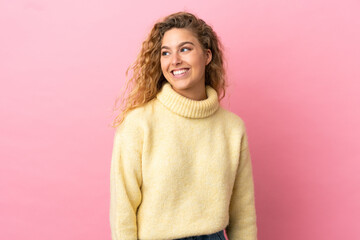 Young blonde woman isolated on pink background looking side