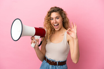 Young blonde woman isolated on pink background holding a megaphone and showing ok sign with fingers