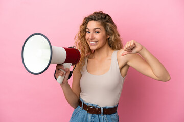 Young blonde woman isolated on pink background holding a megaphone and proud and self-satisfied