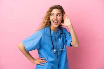 Young surgeon doctor woman isolated on pink background listening to something by putting hand on the ear