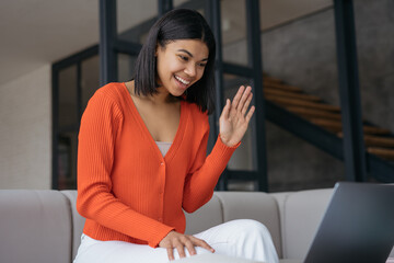 Happy influencer using laptop recording video waving hand talking with subscribers. Beautiful smiling African American woman freelancer having video call working online from home. Successful business 