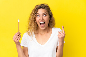 Young caucasian woman holding a brushing teeth isolated on yellow background thinking an idea pointing the finger up