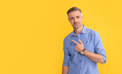 smiling mature man with wrist watch point finger on yellow background, copy space, business hours