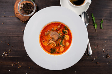 Hot soup with meat and mushrooms in a white plate on wooden background
