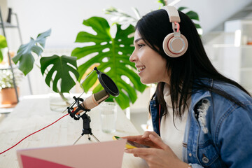 beautiful hispanic woman recording a podcast with microphone and headphones from home, -...