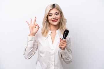 Young singer woman picking up a microphone isolated on white background showing ok sign with fingers