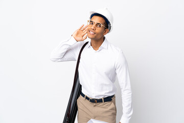 African American architect man with helmet and holding blueprints over isolated white background _ listening to something by putting hand on the ear