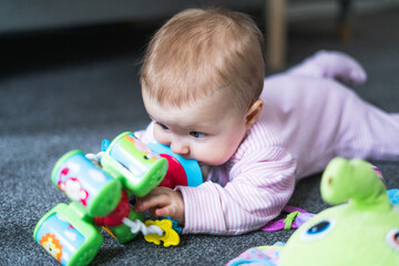 Small 5-month old baby girl lying on the floor, playing with toys