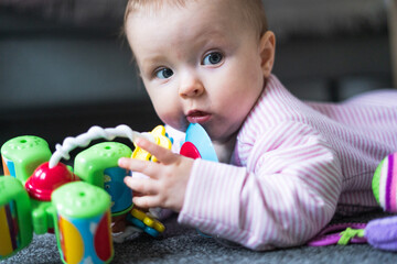 Small 5-month old baby girl lying on the floor, playing with toys