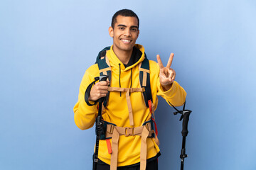 African American man with backpack and trekking poles over isolated background smiling and showing victory sign