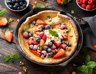 Dutch baby pancake with berries and icing sugar in a iron cast pan. Morning breakfast
