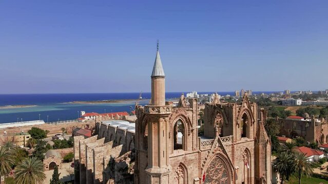Aerial 4k Lala Mustafa Pasha Camii Mosque or Old Cathedral of Saint Nicholas medieval building with minaret in Famagusta, North Cyprus historical city centre, clear blue sky in sunny day, Cyprus