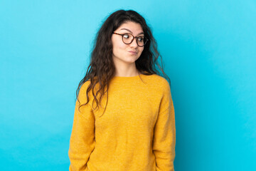 Teenager Russian girl isolated on blue background making doubts gesture looking side