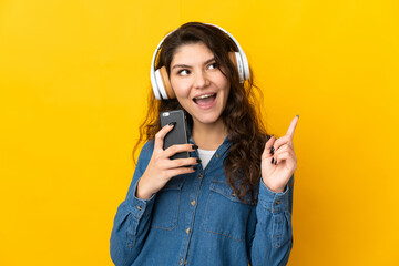 Teenager Russian girl isolated on yellow background listening music with a mobile and singing