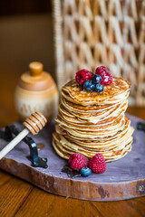Delicious pancakes with honey, blueberries and raspberries. Next to it is a wooden barrel with an...