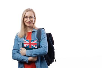 Smiling caucasian woman holding english flag and book while standing over white background. Female student in eyewear with backpack posing in studio.