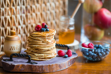 Delicious pancakes with honey, blueberries and raspberries. Next to it is a wooden barrel with an inscription in Russian: 