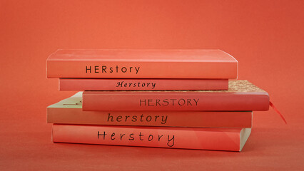 Herstory titles in pile of books. Red book spines on red background. Feminism and female history concept.