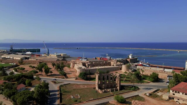 Aerial 4k Othello Castle medieval building in Famagusta Walled City in North Cyprus which is surrounded with old town streets, sea port and touristic attractions with blue sky in sunny day, Cyprus