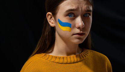 Flag of Ukraine painted on a face on the face of a teenage child. War between Ukraine and Russia. Crying girl with a face art.