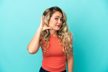 Naklejka premium Young Brazilian woman isolated on blue background listening to something by putting hand on the ear