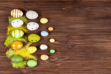 Happy Easter concept. Colorful Easter eggs with bright feathers on a dark wooden background. View from above. Place for inscription, text. Basis for a postcard.