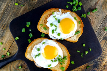 Fried egg sandwich with yolk, chili pepper on toasted slice of bread sprinkled with green onions. Selective focus. Top view. - 493775351