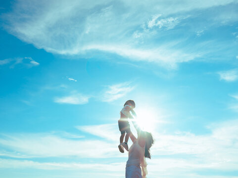 Mother playing with baby boy,mom raises the child in her arms up with blue sky.