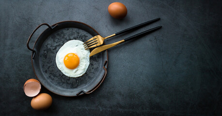 Bannner.Homemade fried egg in a vintage pan and stylish cutlery on a dark background. View from above. Copy space for text.