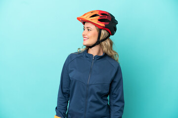 Young cyclist woman isolated on blue background looking to the side and smiling