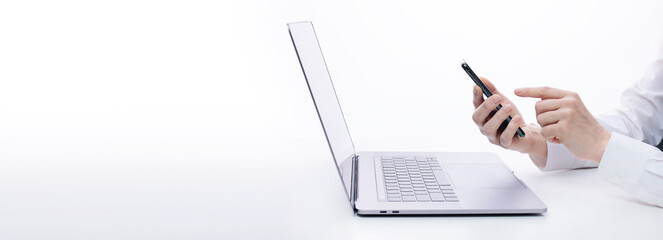 Close up of woman sitting in white studio with wireless laptop and using modern smartphone. Technology for work and business.