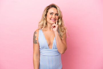 Young Brazilian woman in swimsuit in summer holidays isolated on pink background thinking an idea while looking up