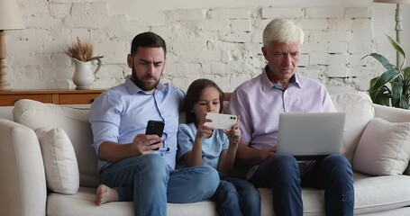 Multigenerational men, family sit on sofa use diverse devices. Granddad, his grown up son, little grandson spend time at home absorbed in wireless gadgets usage. New apps, modern tech overuse concept