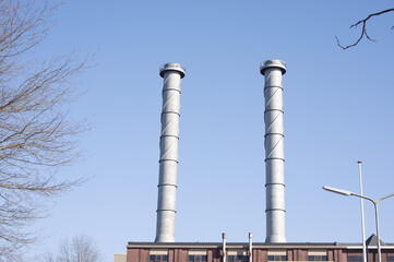 Top of a factory with two industrial chimneys with a clear blue sky in the Netherlands