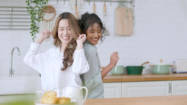 LGBTQ Asian couple or lesbian or friend dancing and having fun at home kitchen and showing love to each other smiling and laughing happily on holiday