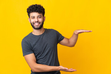Young Moroccan man isolated on yellow background holding copyspace to insert an ad