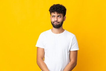 Young Moroccan man isolated on yellow background having doubts while looking up