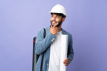 Young architect Moroccan man with helmet and holding blueprints over isolated background looking up...