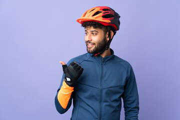 Young Moroccan cyclist man isolated on purple background pointing to the side to present a product