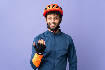 Young Moroccan cyclist man isolated on purple background inviting to come with hand. Happy that you came - obrazy, fototapety, plakaty
