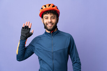Young Moroccan cyclist man isolated on purple background saluting with hand with happy expression - obrazy, fototapety, plakaty