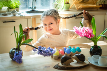 Obraz na płótnie Canvas a little cute girl paints Easter eggs. spring flowers hyacinths, colorful eggs - holiday decoration
