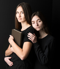 gentle portrait of 2 young girls-girlfriends with a book in their hands on a dark background close-up