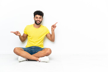 Young Moroccan handsome man sitting on the floor over isolated background pointing finger to the laterals and happy